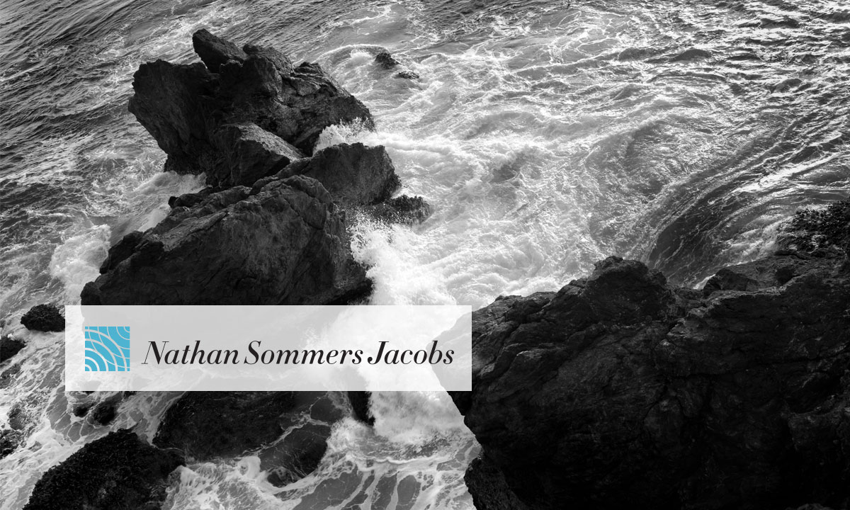 Waves crashing over rocks with the Nathan Sommers Jacobs banner.