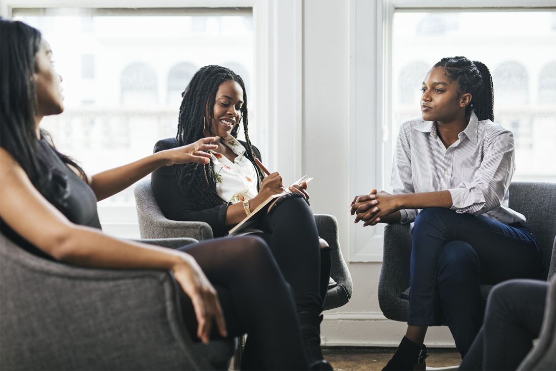 Three people holding a discussion in black chairs