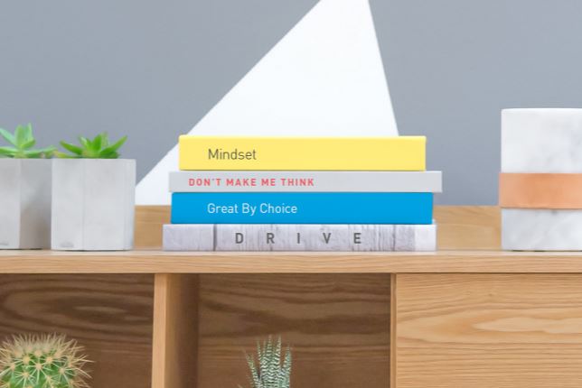 Three books stacked on a shelf surrounded by plants.