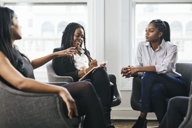 Three people holding a discussion in black chairs