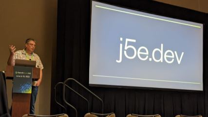 Donovan standing in front of his presentation screen at OpenJS World, with a slide that says "j5e.dev"
