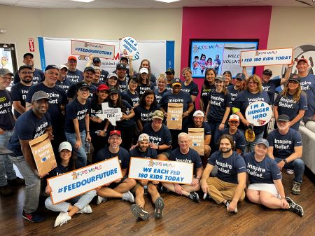 Entire BE team gathered in a colorful room holding signs from Kids' meals talking about the amount of meals we prepared