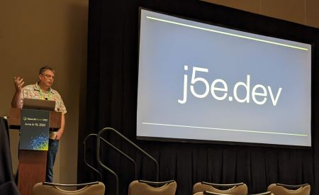 Donovan standing in front of his presentation screen at OpenJS World, with a slide that says "j5e.dev"