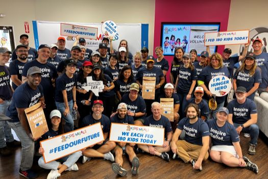 Entire BE team gathered in a colorful room holding signs from Kids' meals talking about the amount of meals we prepared