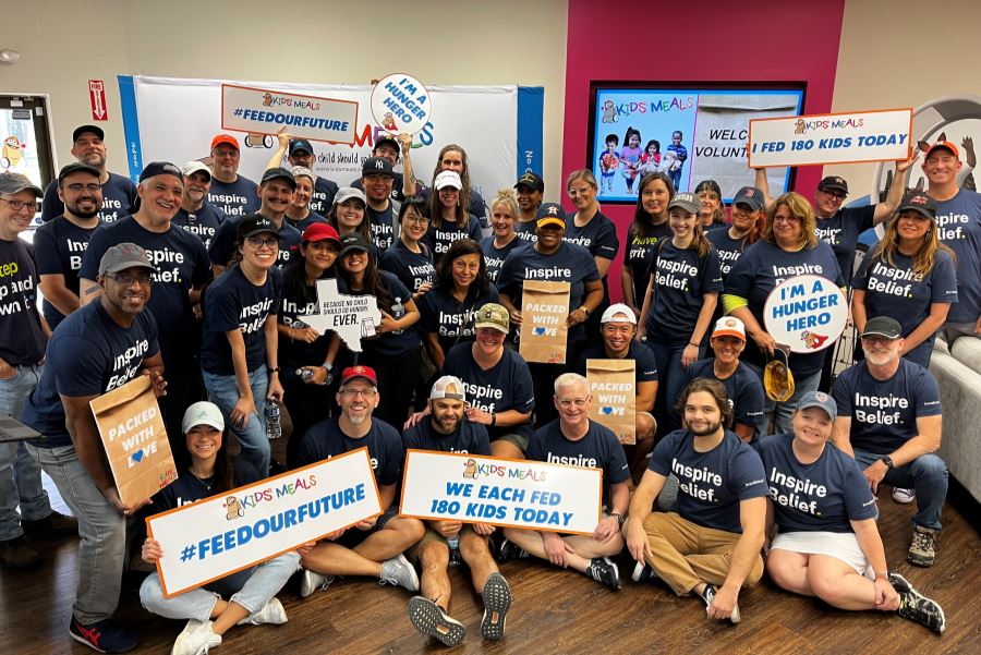 Entire BE team gathered in a colorful room holding signs from Kids' meals talking about the amount of meals we prepared