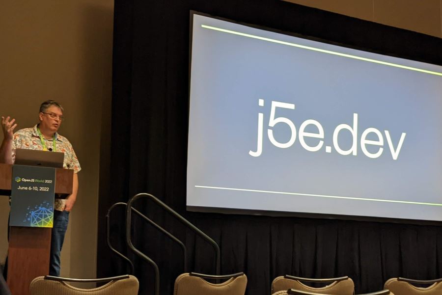 Donovan standing in front of his presentation screen at OpenJS World, with a slide that says "j5e.dev"