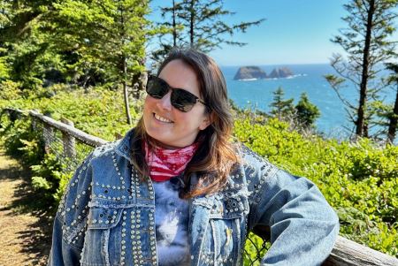 Emily standing outside in front of some trees and a coastline