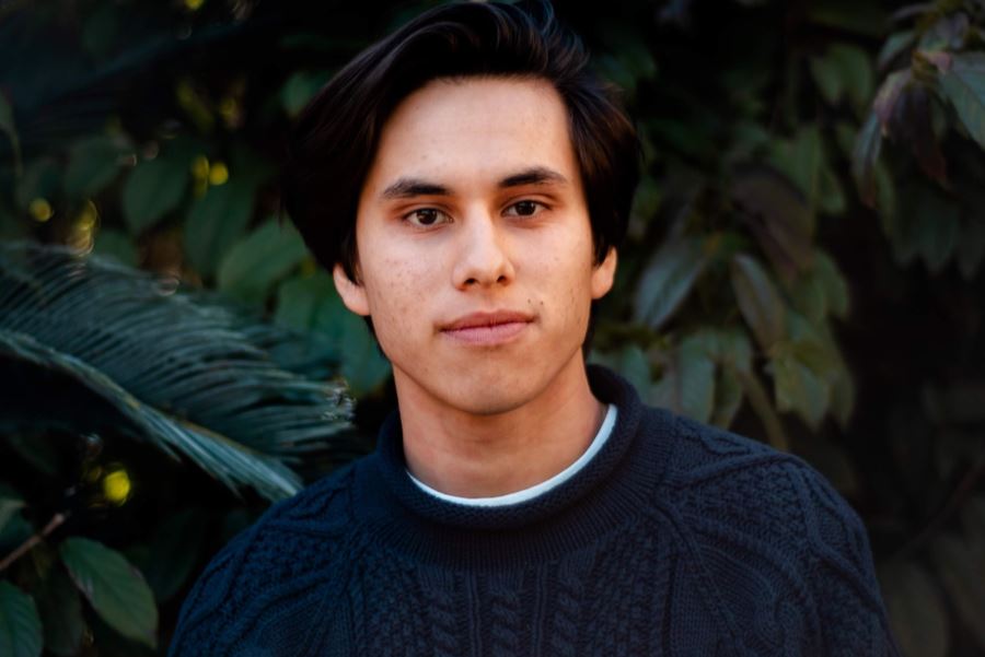 A close-up photo of Krzysztof wearing a blue sweater on a background of green foliage