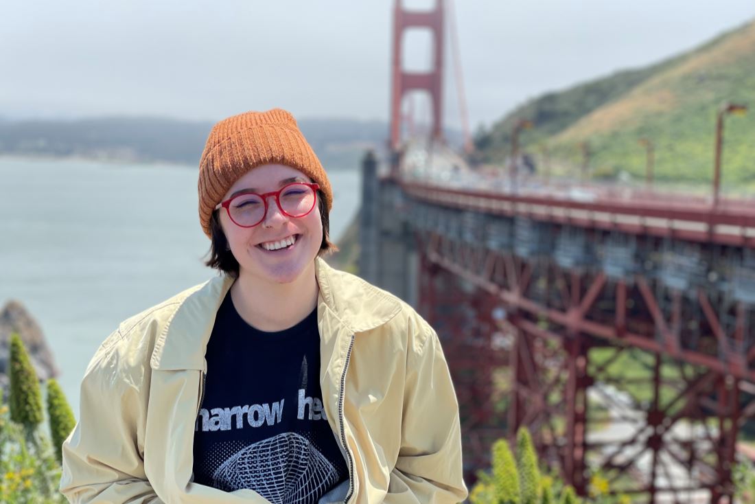Haley wearing a yellow jacket and an orange beanie in San Francisco with the golden gate bridge in the background