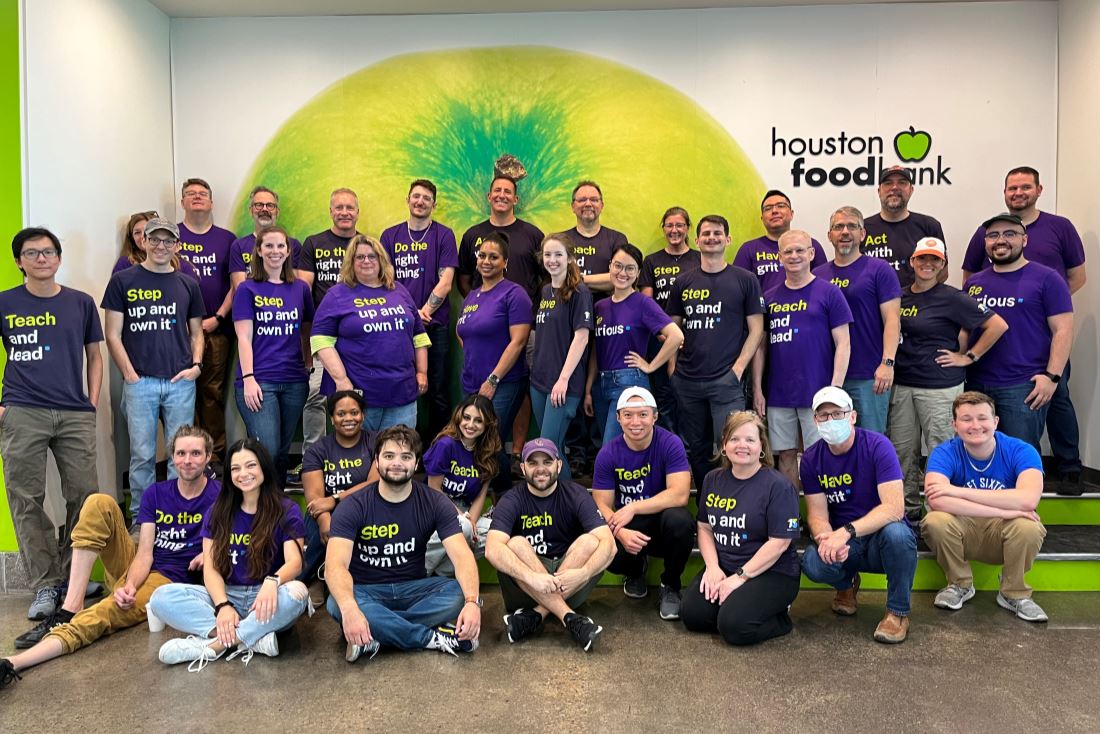 entire BE team, wearing purple t-shirst, in front of a green backdrop at the Houston Food Bank
