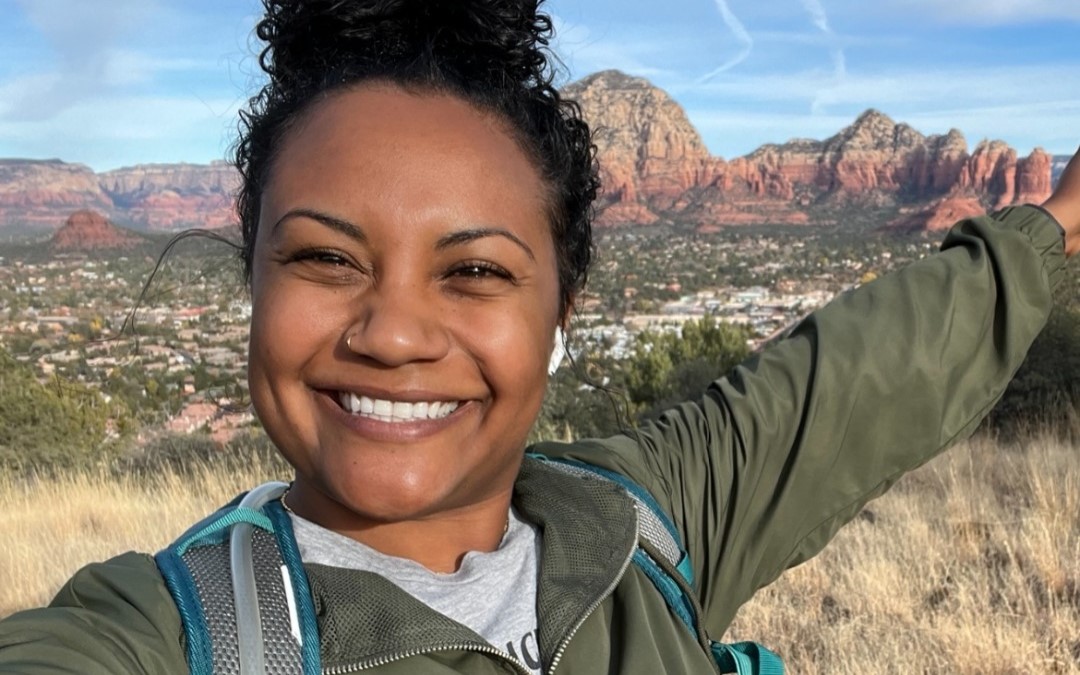 Kameshia wearing a green jacket on a mountain in front of a huge vista with orange and brown mesas