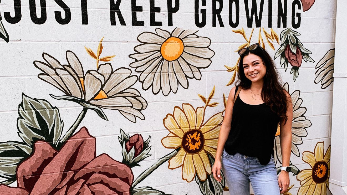 Sasha standing in front of a decorative wall with the text "Just Keep Growing"