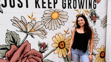 Sasha standing in front of a decorative wall with the text "Just Keep Growing"