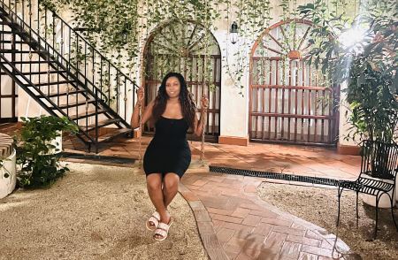 Denajia sitting in a courtyard on a rope swing, with green foliage behind her