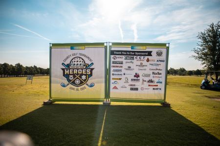Large panel with charity event graphics on a golf course with sun shining in the background