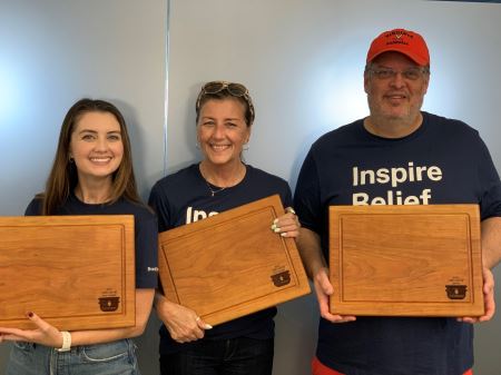 Maeghan, Laura E and Donovan standing in front of a frosted glass window holding their awards for the Chili Cookoff