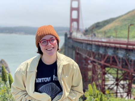 Haley wearing a yellow jacket and an orange beanie in San Francisco with the golden gate bridge in the background