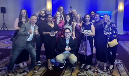 A group of 14 BrandExtract employees standing in a group in an event center, holding up their awards form the 2023 Crystal Awards.