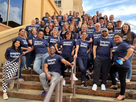 A photo of the entire BrandExtract team wearing navy-blue tshirts with "Inspire Belief" on them, posing on a staircase outside