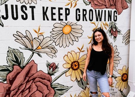 Sasha standing in front of a decorative wall with the text "Just Keep Growing"