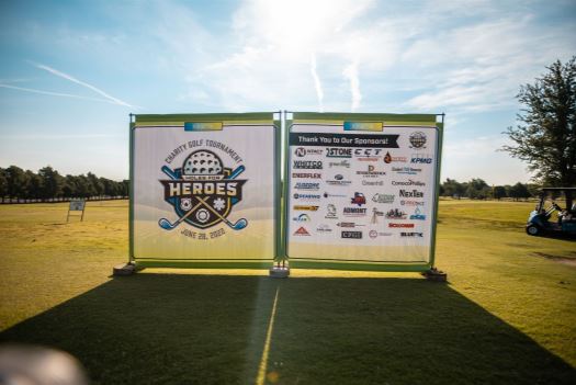 Large panel with charity event graphics on a golf course with sun shining in the background