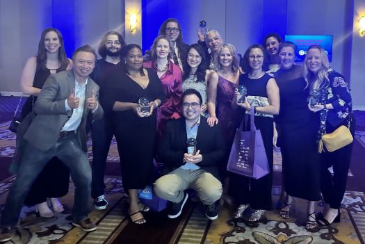 A group of 14 BrandExtract employees standing in a group in an event center, holding up their awards form the 2023 Crystal Awards.