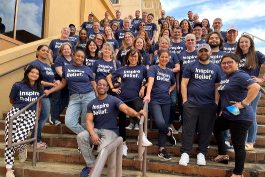 A photo of the entire BrandExtract team wearing navy-blue tshirts with "Inspire Belief" on them, posing on a staircase outside