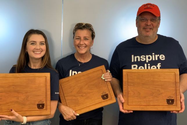 Maeghan, Laura E and Donovan standing in front of a frosted glass window holding their awards for the Chili Cookoff