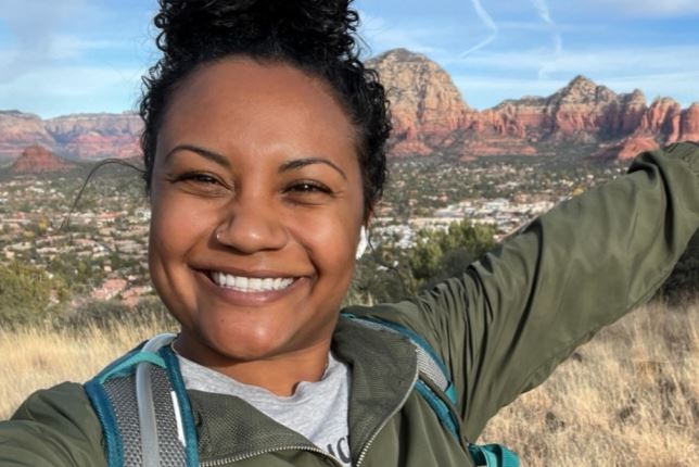 Kameshia wearing a green jacket on a mountain in front of a huge vista with orange and brown mesas