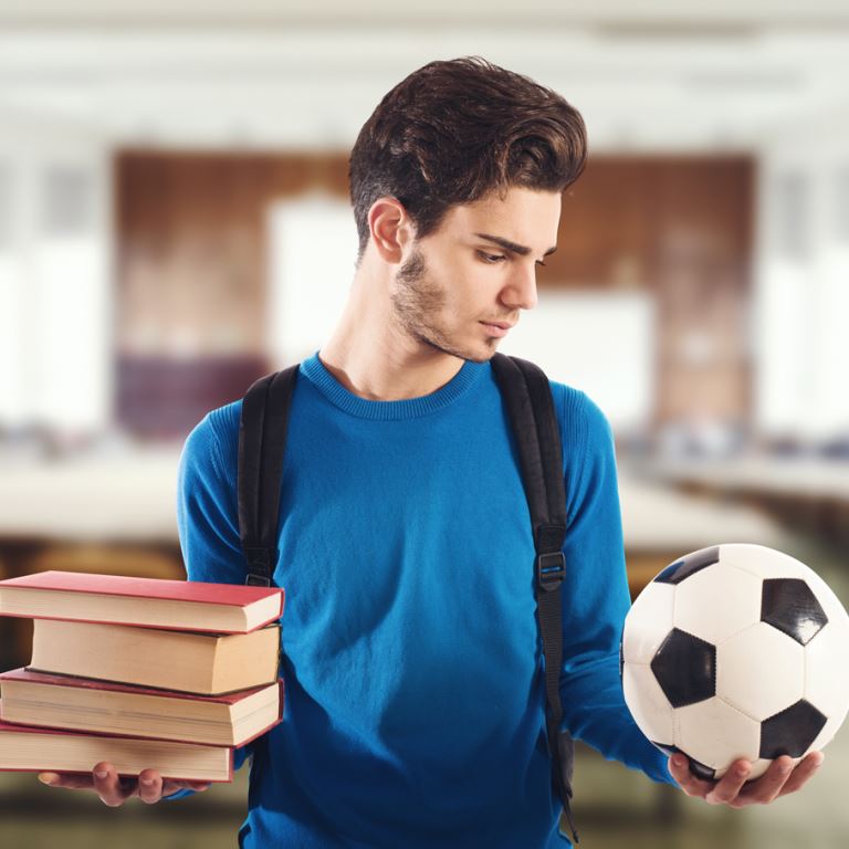 Student-athlete deciding between a stack of books and a soccer ball.