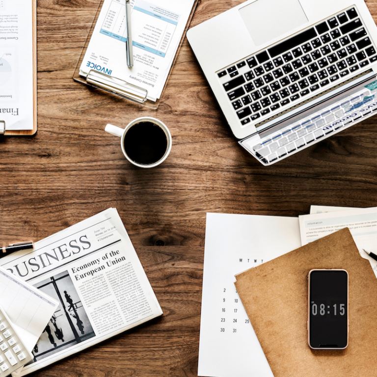 Overhead view of a desk with papers and coffee and a laptop