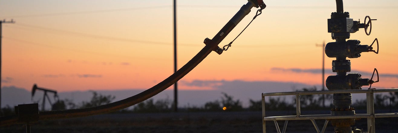 Oilfield equipment and piping silhouetted against an orange and purple sunset sky.