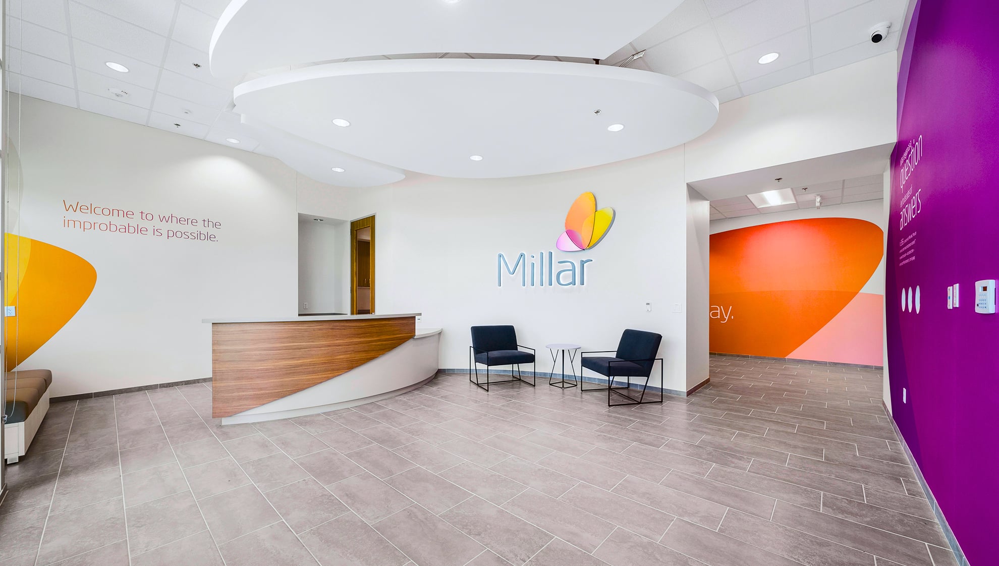 Millar reception lobby with branded wall graphics, welcome message ‘Welcome to where the improbable is possible,’ and modern seating area.