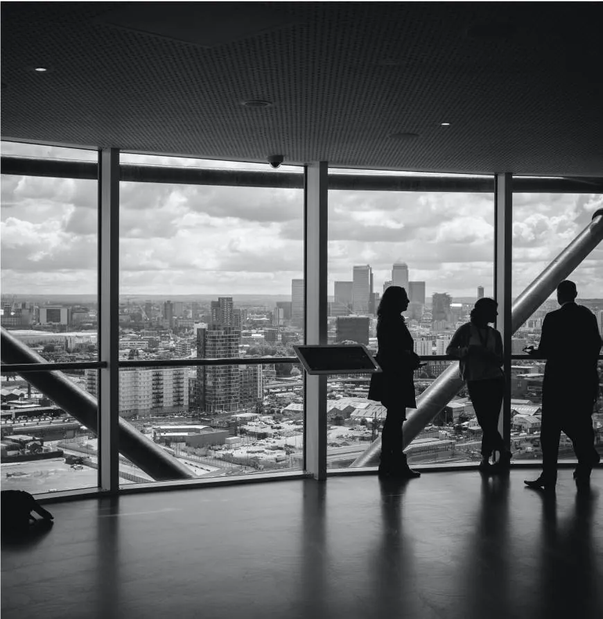 A black and white photograph of people standing in a penthouse suite of a tall building, looking out the window