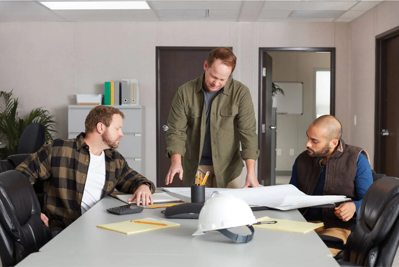 Construction managers and engineers looking over plans at a conference table in a temporary space from WillScot
