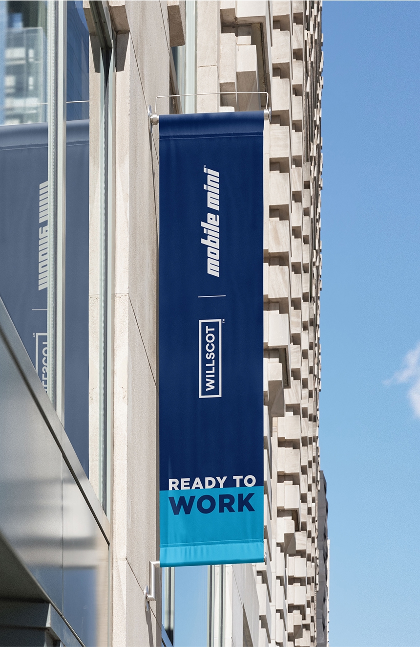 A blue WillScot Mobile Mini banner hanging out side of a building