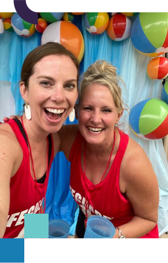 Laura and Kristen laughing wearing lifeguard shirts in front of a wall of beach balls