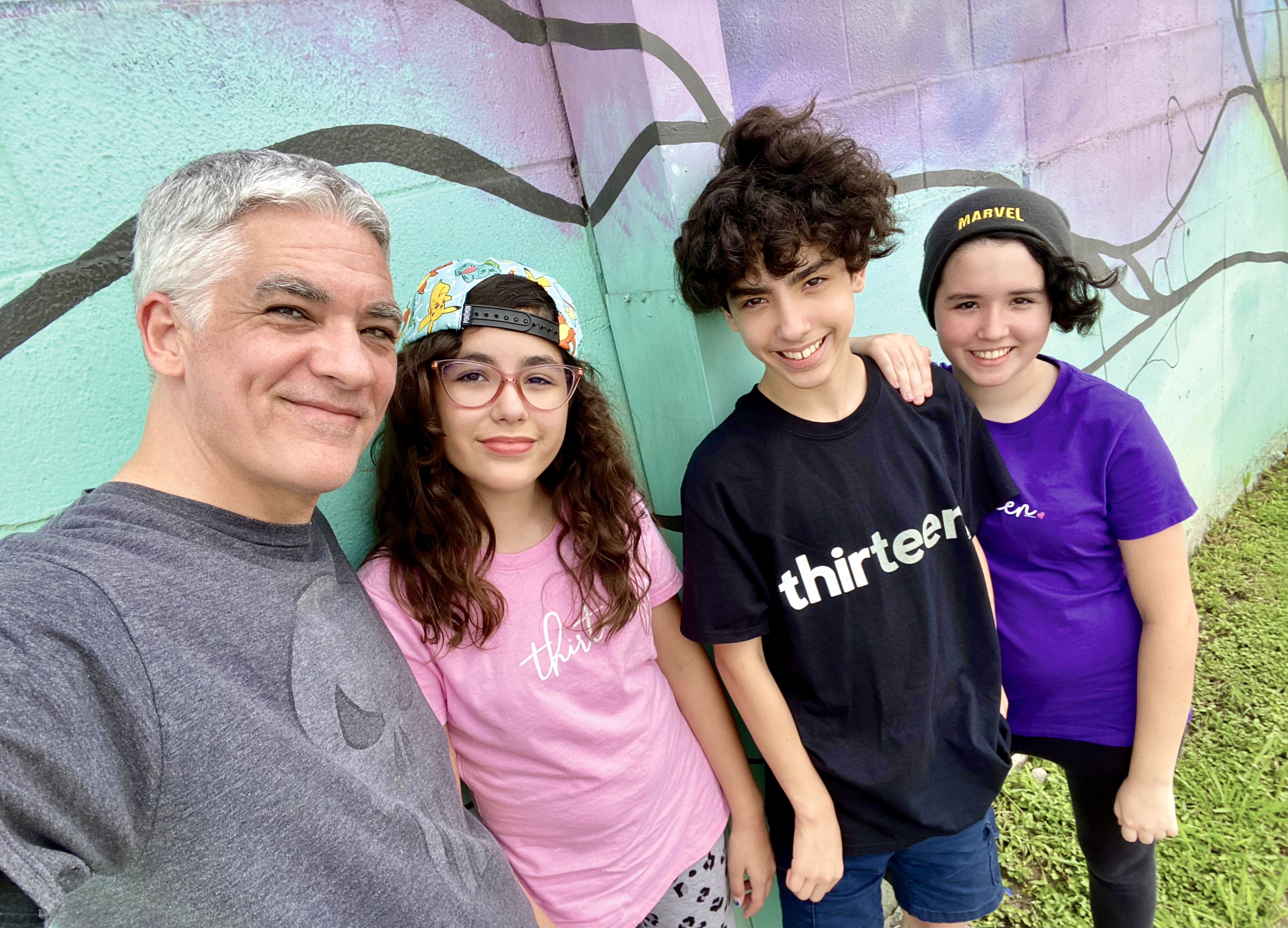 Adrian posing with his three kids in front of a teal and purple background