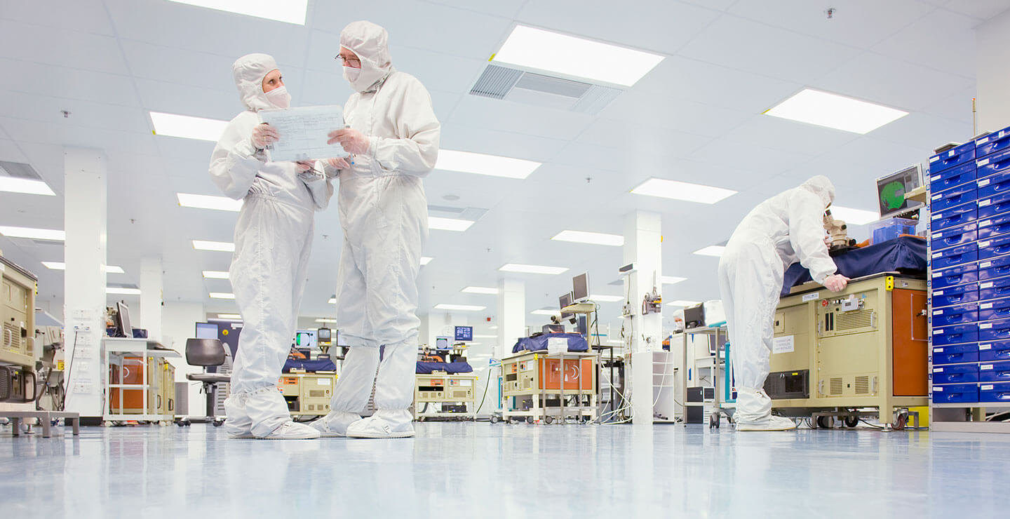 A wide shot of Millar Scientists in a giant manufacturing lab looking over papers.