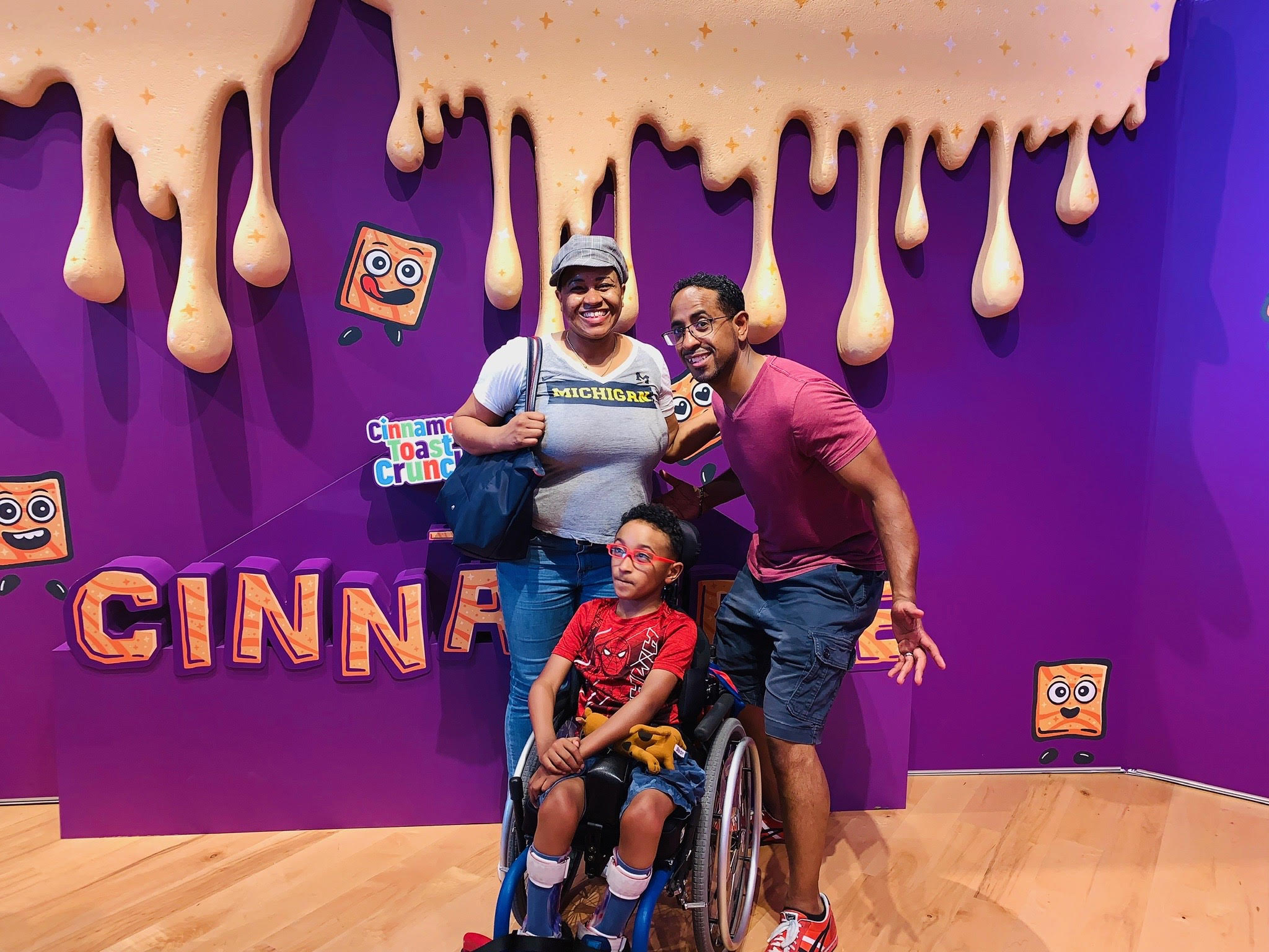 Carleton smiling with his wife and son in front of a cinnamon toast crunch sign