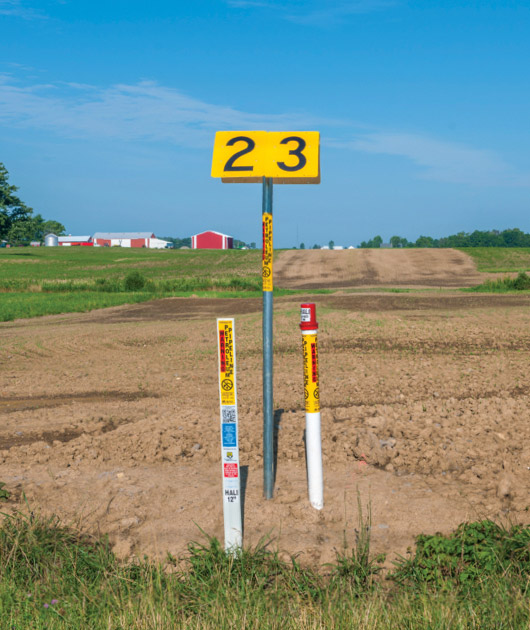 A land marker with pipe line markers next to them in a field