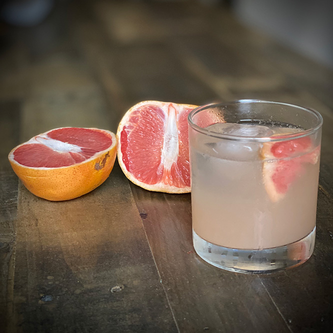 A clear drink with bits of ice in an old-fashioned glass, garnished with a grapefruit slice.