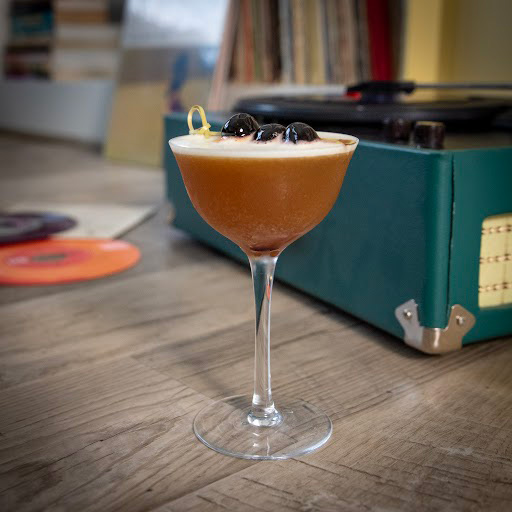 A amber drink in a coupe glass, garnished with three cherries.