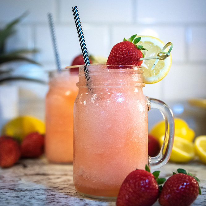 A candy pink drink held in a large mug with a striped straw, garnished with a strawberry.